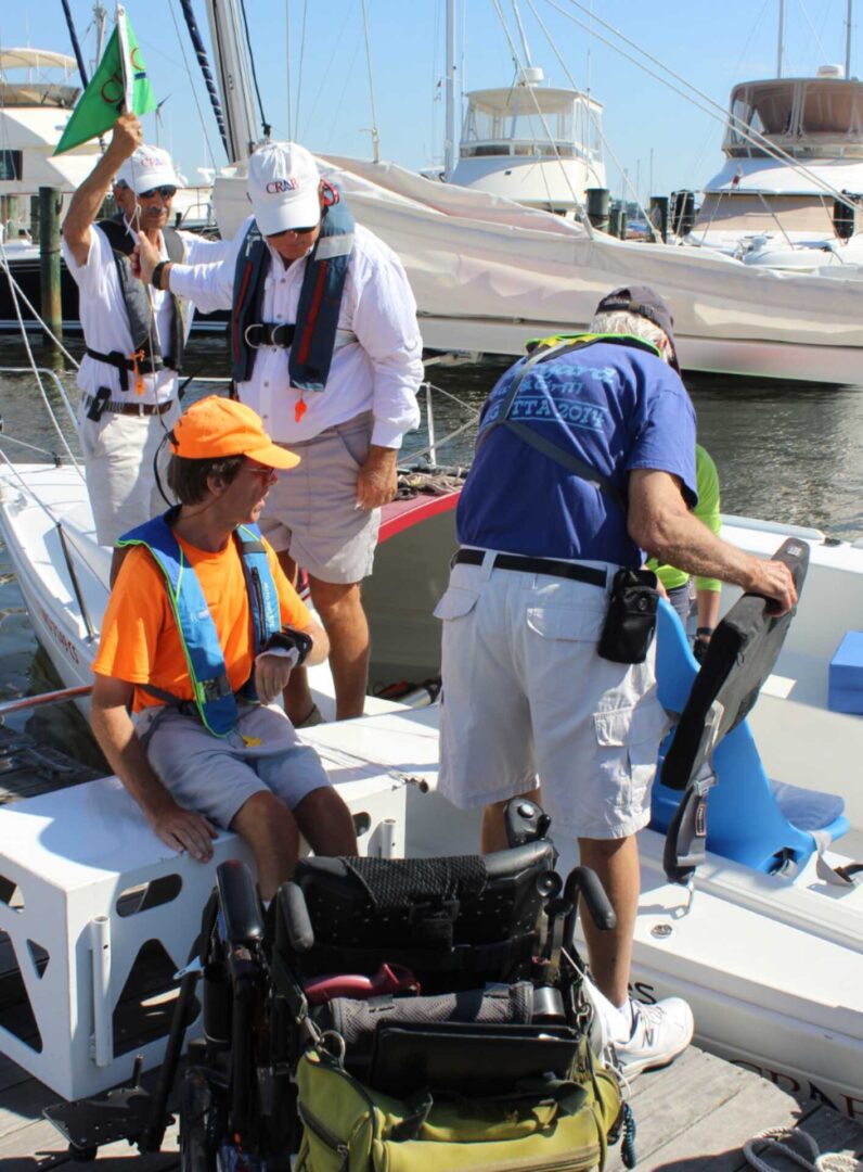 A photo of CRAB volunteers helping guests transfer from their wheelchair to a CRAB sailboat. 
