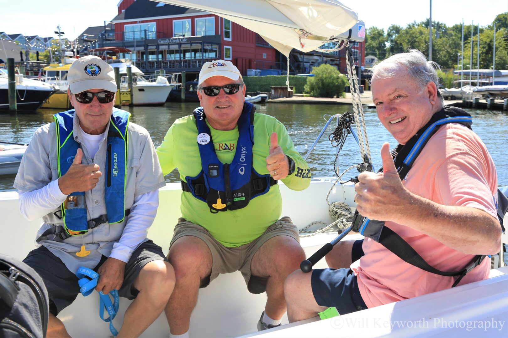 Photo of a CRAB volunteer on a CRAB sailboat with two guests, all three giving a thumbs up and smiling. 