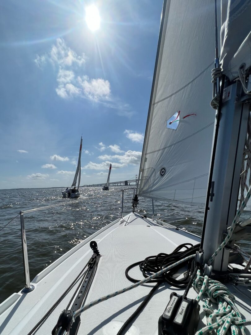 A scenic photo from onboard one of CRAB's sailboats showing two other CRAB boats on the Chesapeake Bay with the sun shining brightly above. 