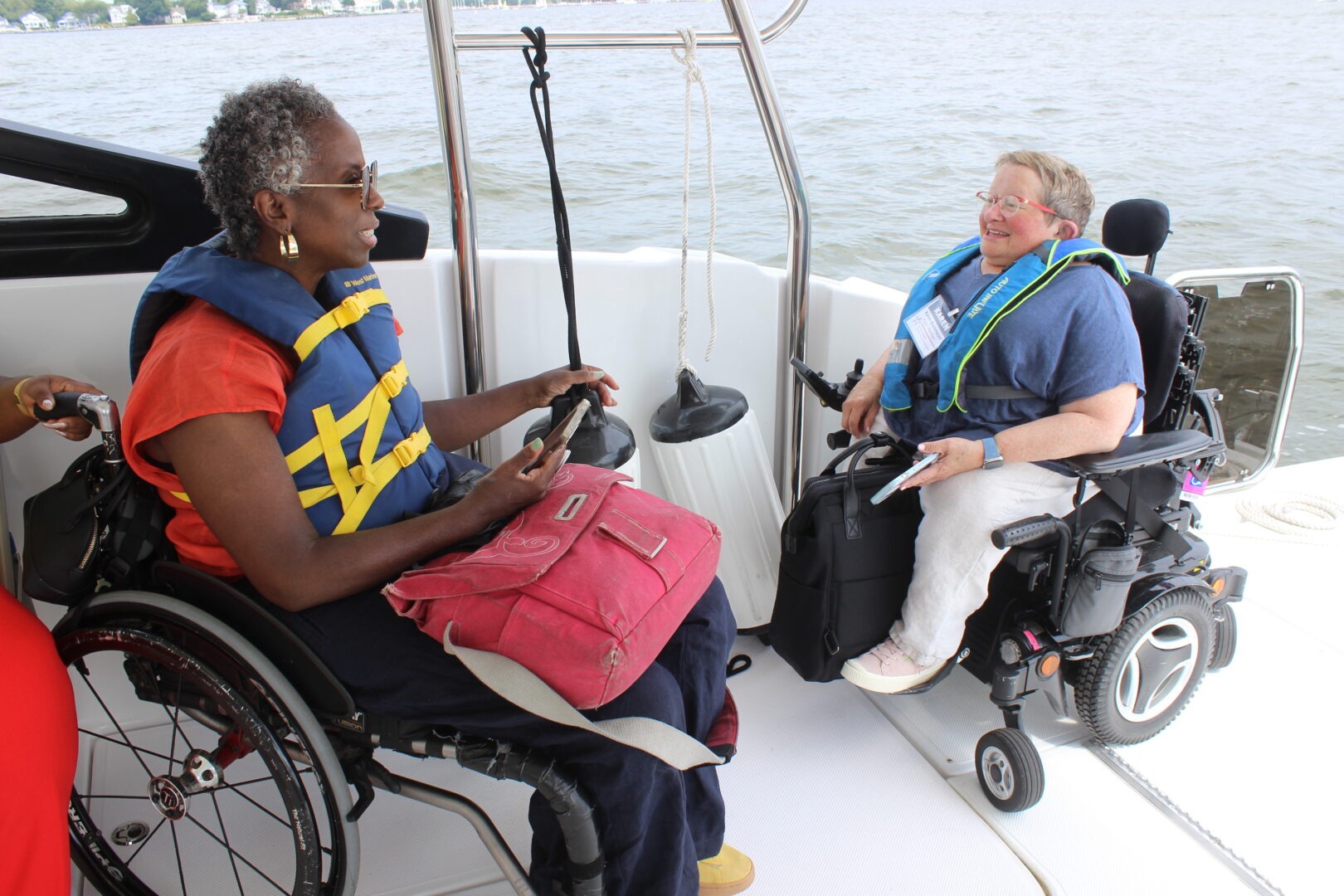 Two women using wheelchairs are smiling and talking onboard the CRAB Gemini power-catamaran.
